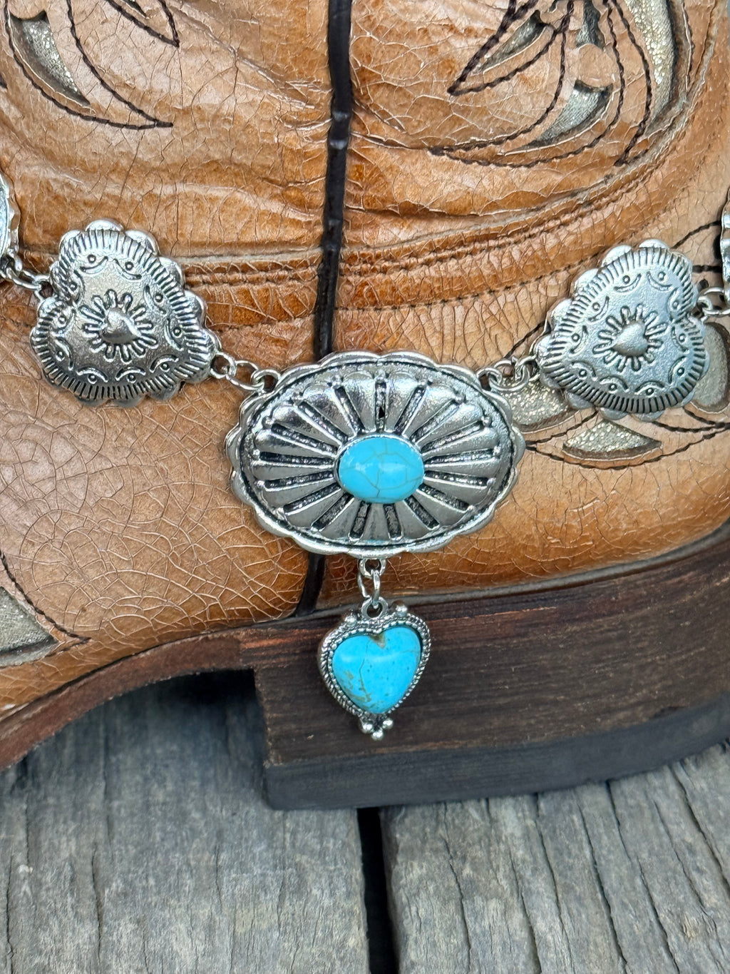 Detail view of large oval silver sunburst concho with turquoise cabochon center stone and turquoise heart charm pendant drop on silver concho chain boot bracelet
