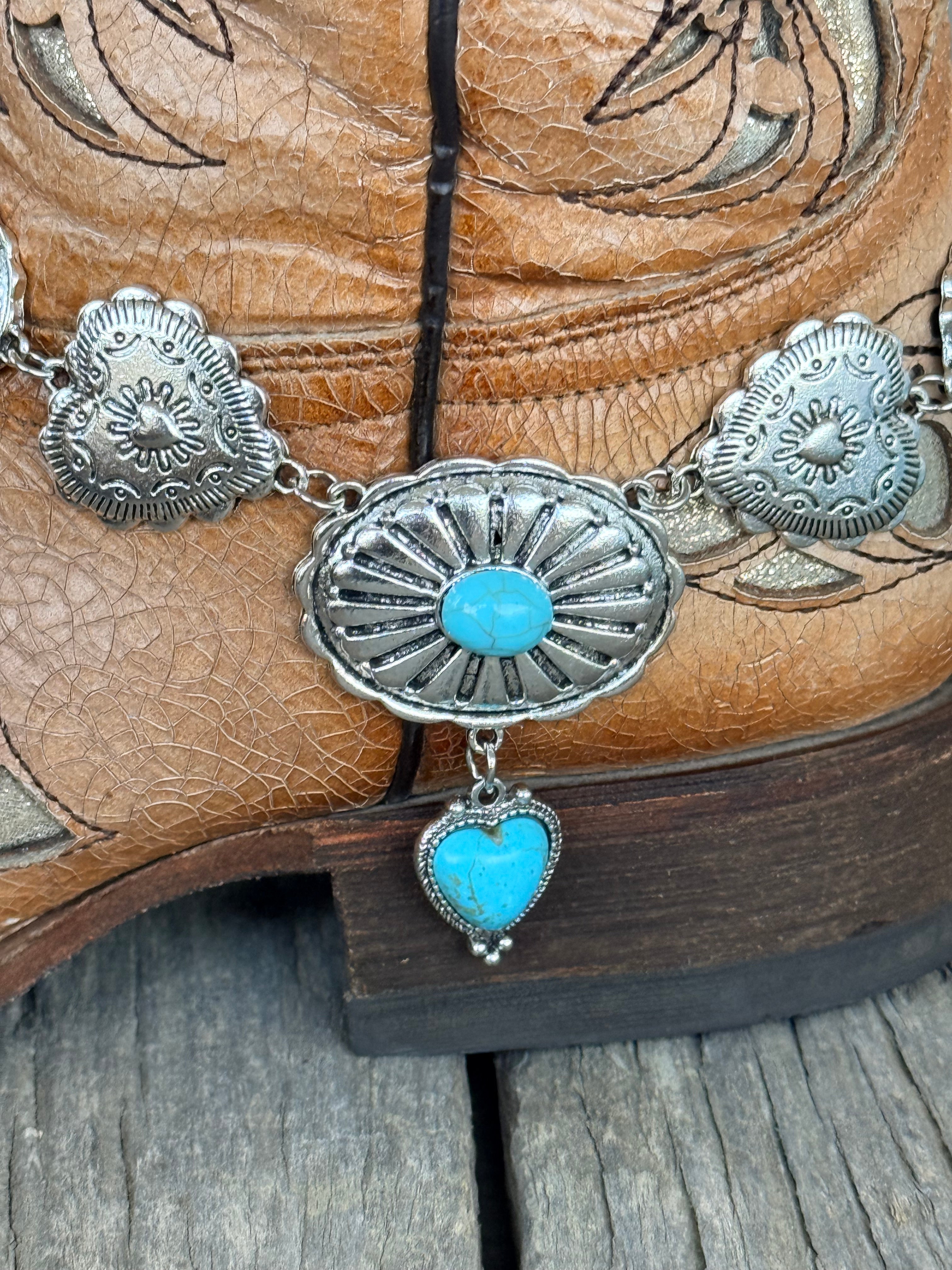 Detail view of large oval silver sunburst concho with turquoise cabochon center stone and turquoise heart charm pendant drop on silver concho chain boot bracelet
