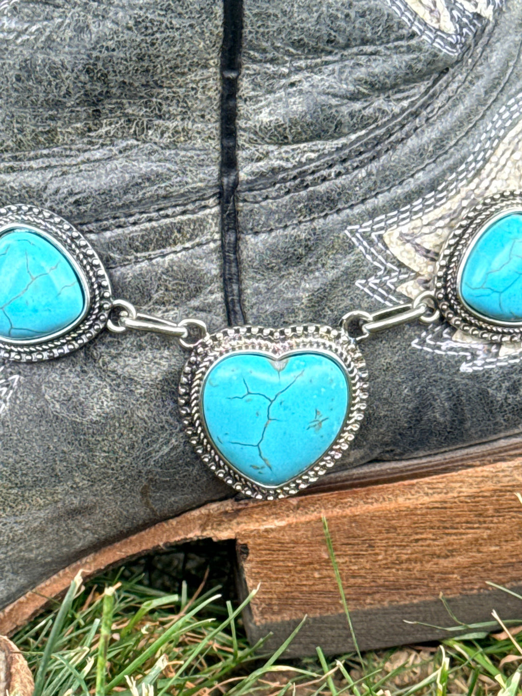 Macro close-up of turquoise howlite heart stone in an ornate silver beaded bezel boot bracelet with graduating heart accent stones and silver link chain on a black cowboy boot
