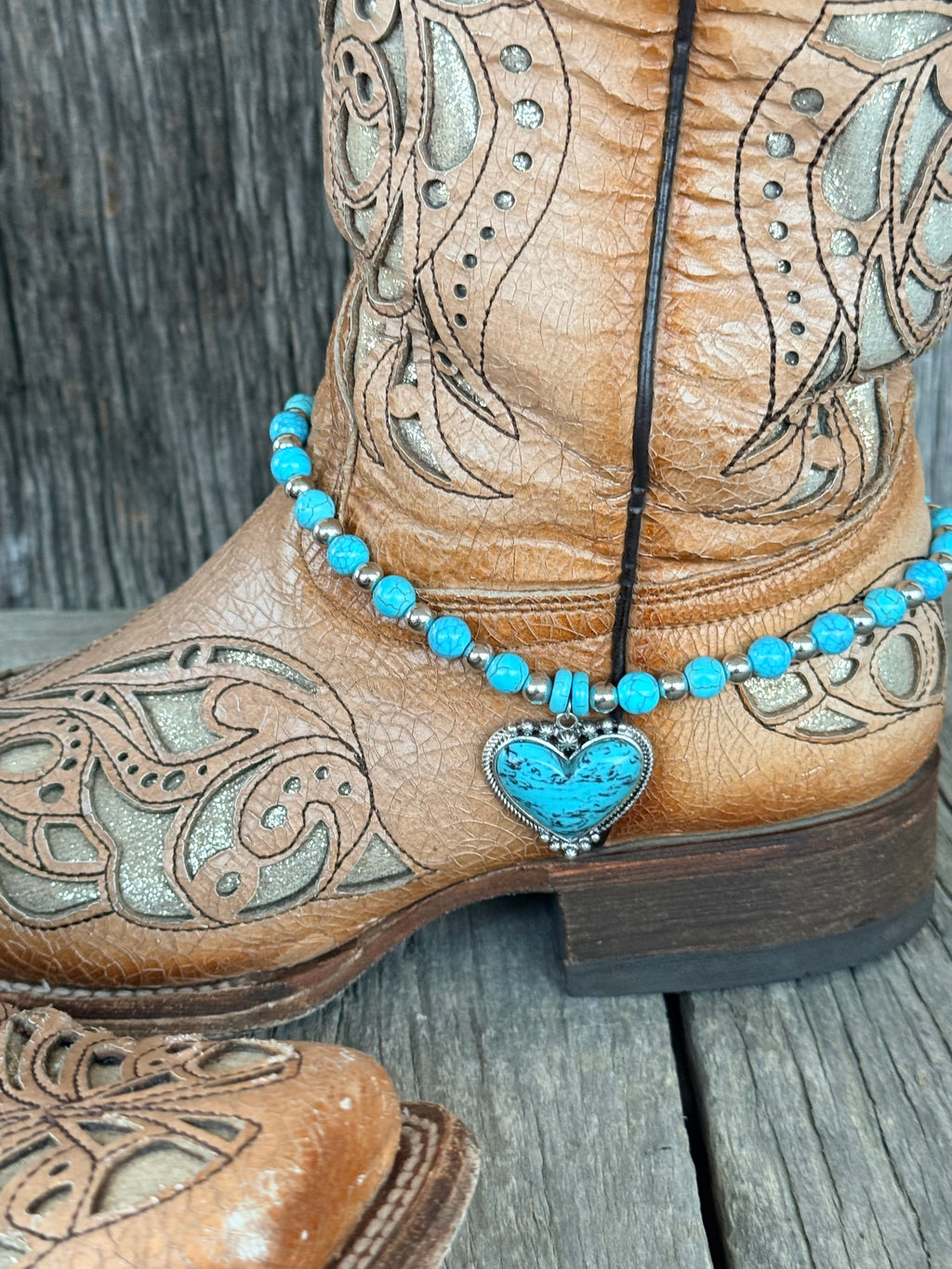 Side angle of turquoise round bead boot bracelet with silver spacers and turquoise heart pendant at ankle of tan tooled leather cowboy boot
