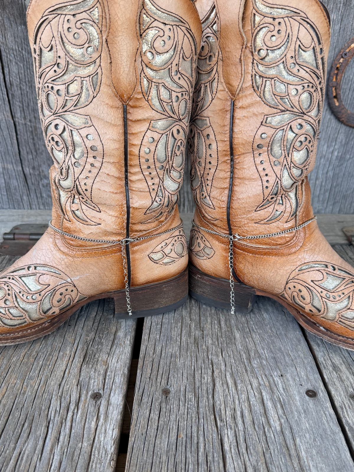 Back view of turquoise squash blossom boot bracelet chain pair on tan tooled leather cowboy boots
