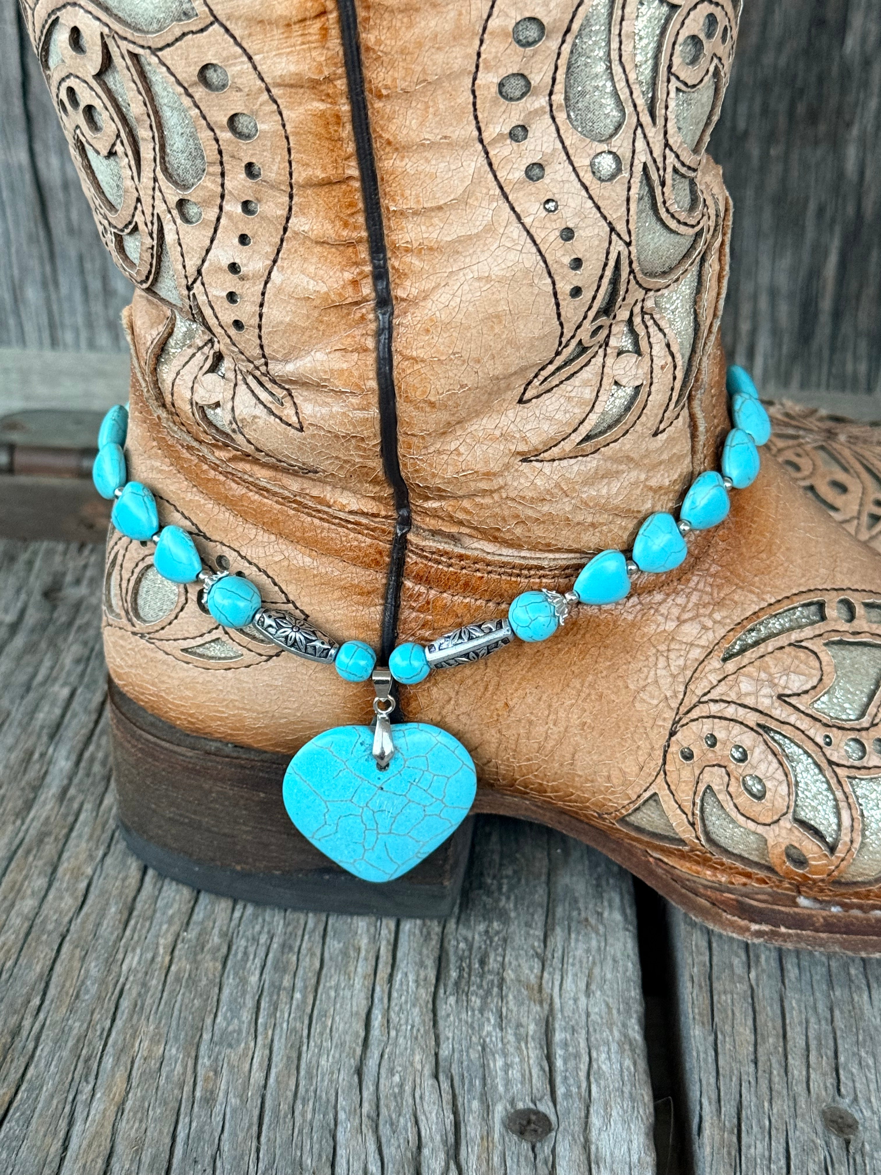 Close-up of turquoise heart bead and silver rondelle boot bracelet with engraved silver tube beads and large crackle turquoise heart stone pendant at heel of tan tooled cowboy boot
