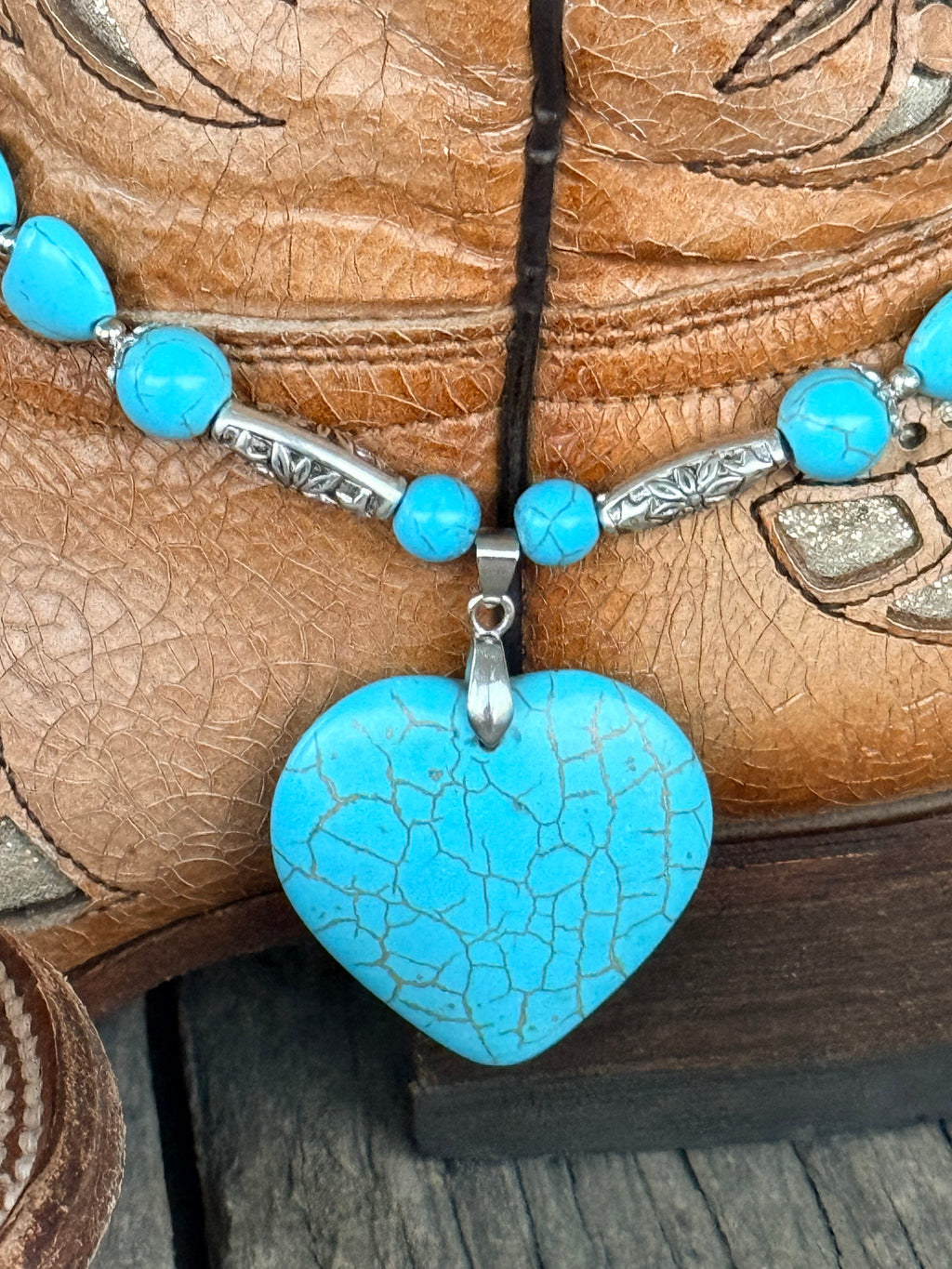Detail close-up of large crackle turquoise heart stone pendant with silver bail and engraved silver floral-stamped tube beads on turquoise heart bead boot bracelet

