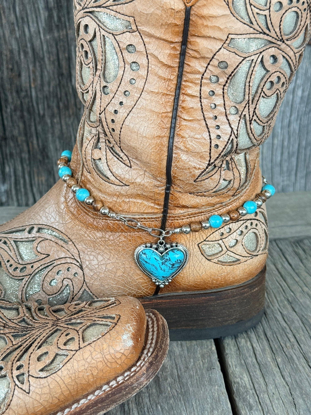 Side angle of turquoise, brown wood and silver beaded boot bracelet with turquoise heart pendant draped at ankle of tan tooled leather cowboy boot
