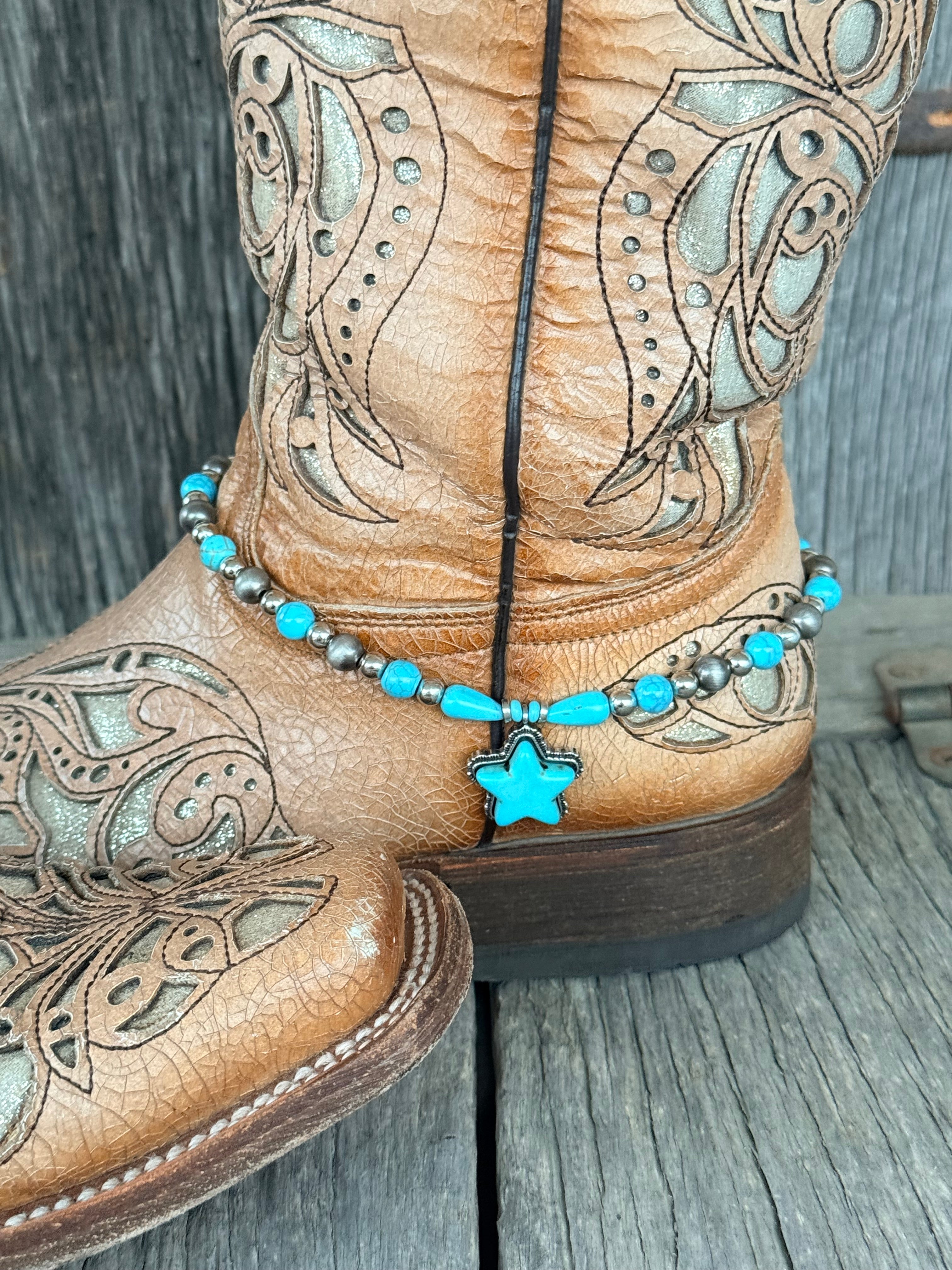 Side view of gunmetal Navajo pearl and turquoise bead boot bracelet with turquoise teardrop beads and large turquoise star stone pendant draping at ankle of tan tooled laser-cut cowboy boot on wood surface
