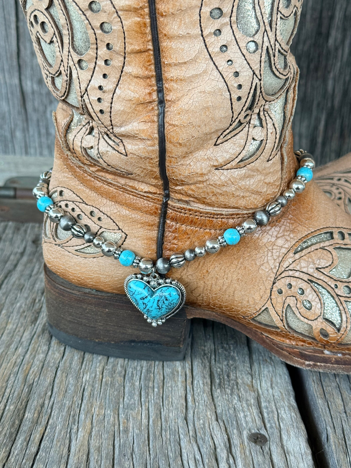 Close-up of turquoise heart pendant in silver dotted bezel on Navajo pearl and turquoise beaded boot bracelet at heel of tan cowboy boot
