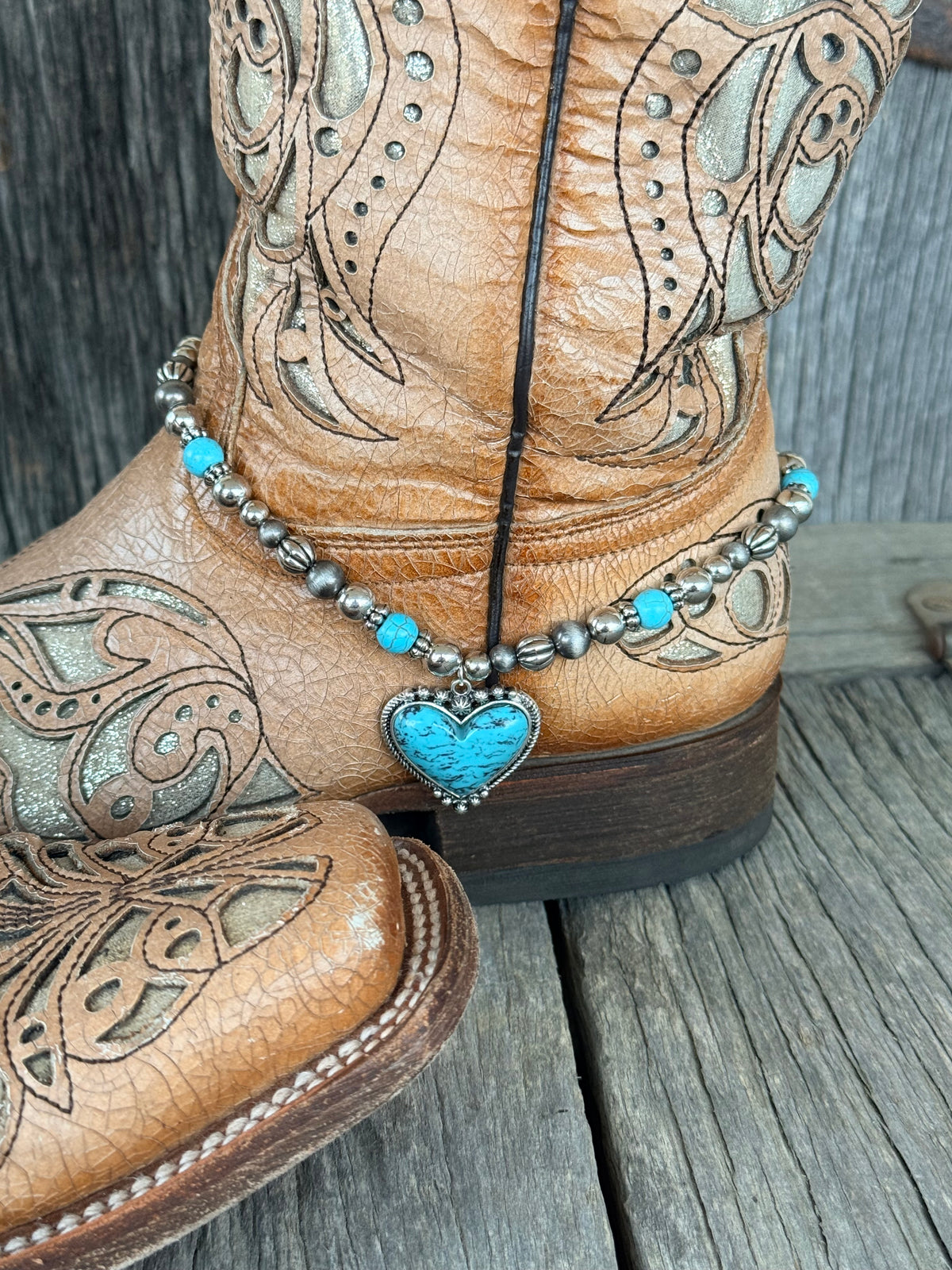 Side angle of Navajo pearl and turquoise beaded boot bracelet with turquoise heart pendant at ankle of tan tooled leather cowboy boot
