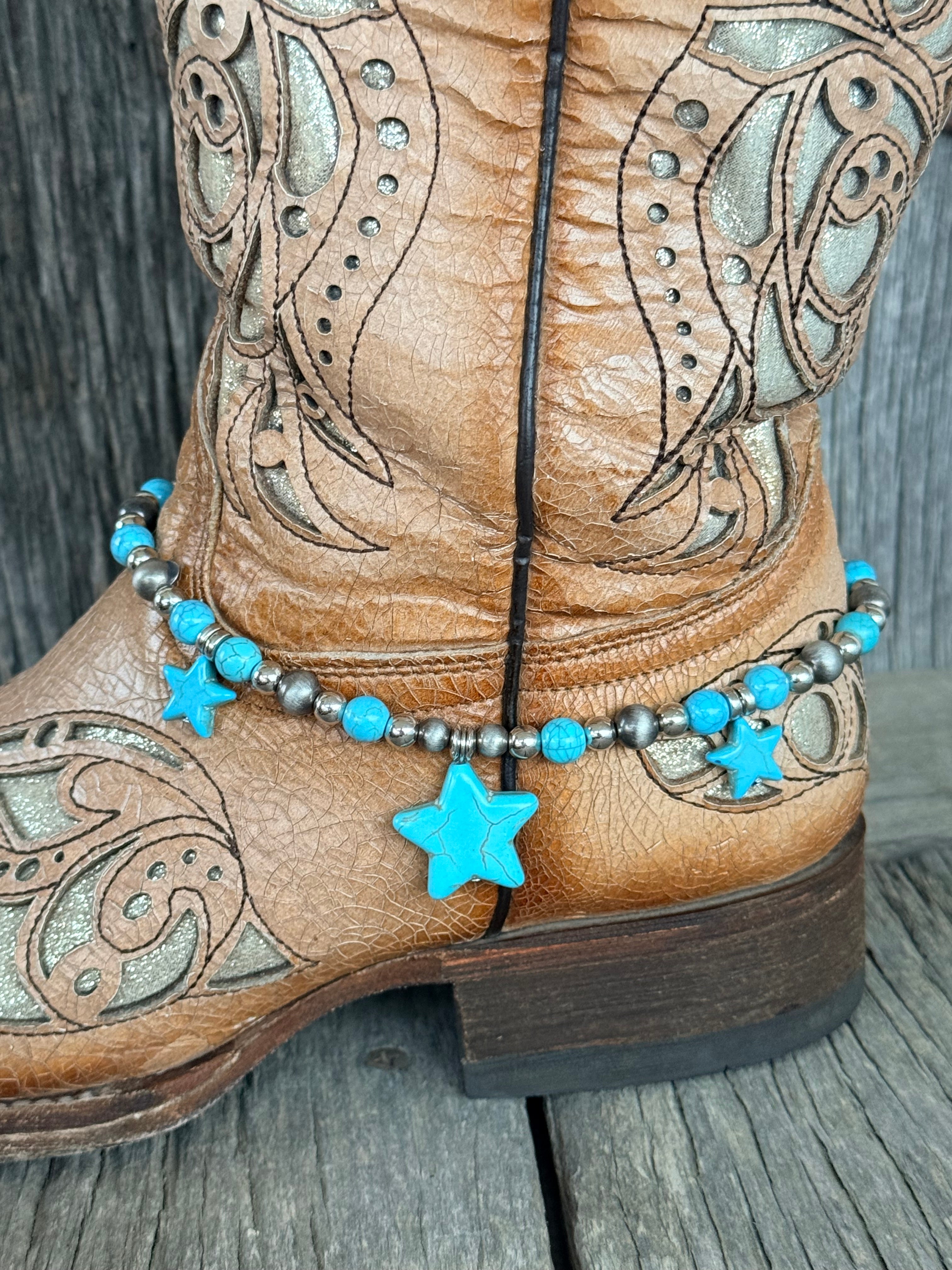 Side view of Navajo pearl and turquoise bead boot bracelet with three turquoise star stone pendants draping at ankle of tan tooled laser-cut cowboy boot on wood surface
