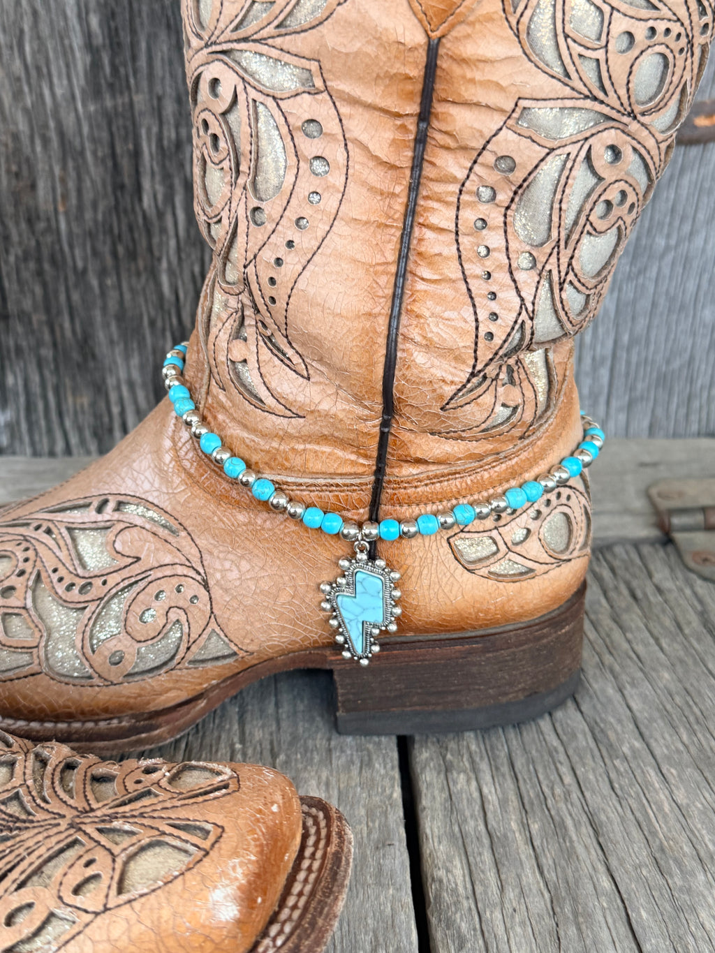 Side angle of turquoise and Navajo pearl silver beaded boot bracelet with lightning bolt pendant draped at ankle of tan tooled leather cowboy boot
