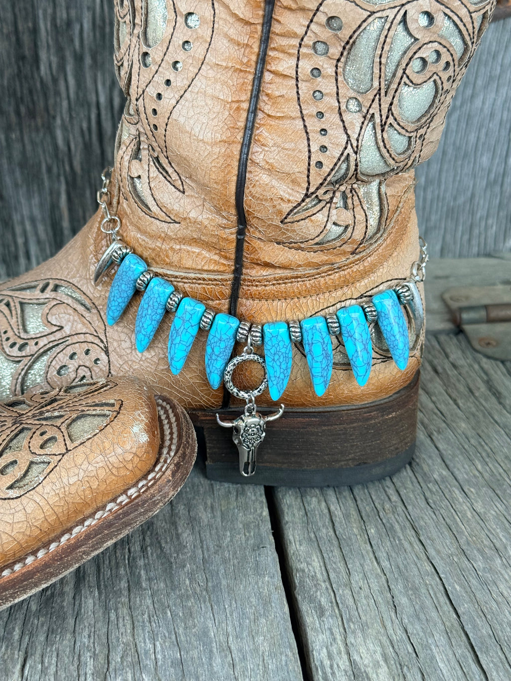 Side angle of turquoise coyote tooth boot bracelet with silver bull skull drop pendant at ankle of tan tooled leather cowboy boot
