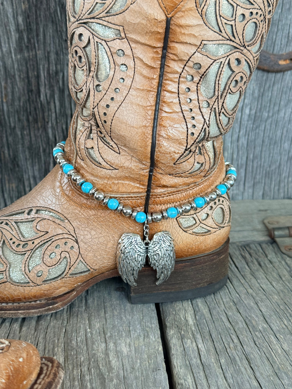 Back view of turquoise and silver beaded boot bracelet with silver angel wing pendant at heel of tan tooled leather cowboy boot
