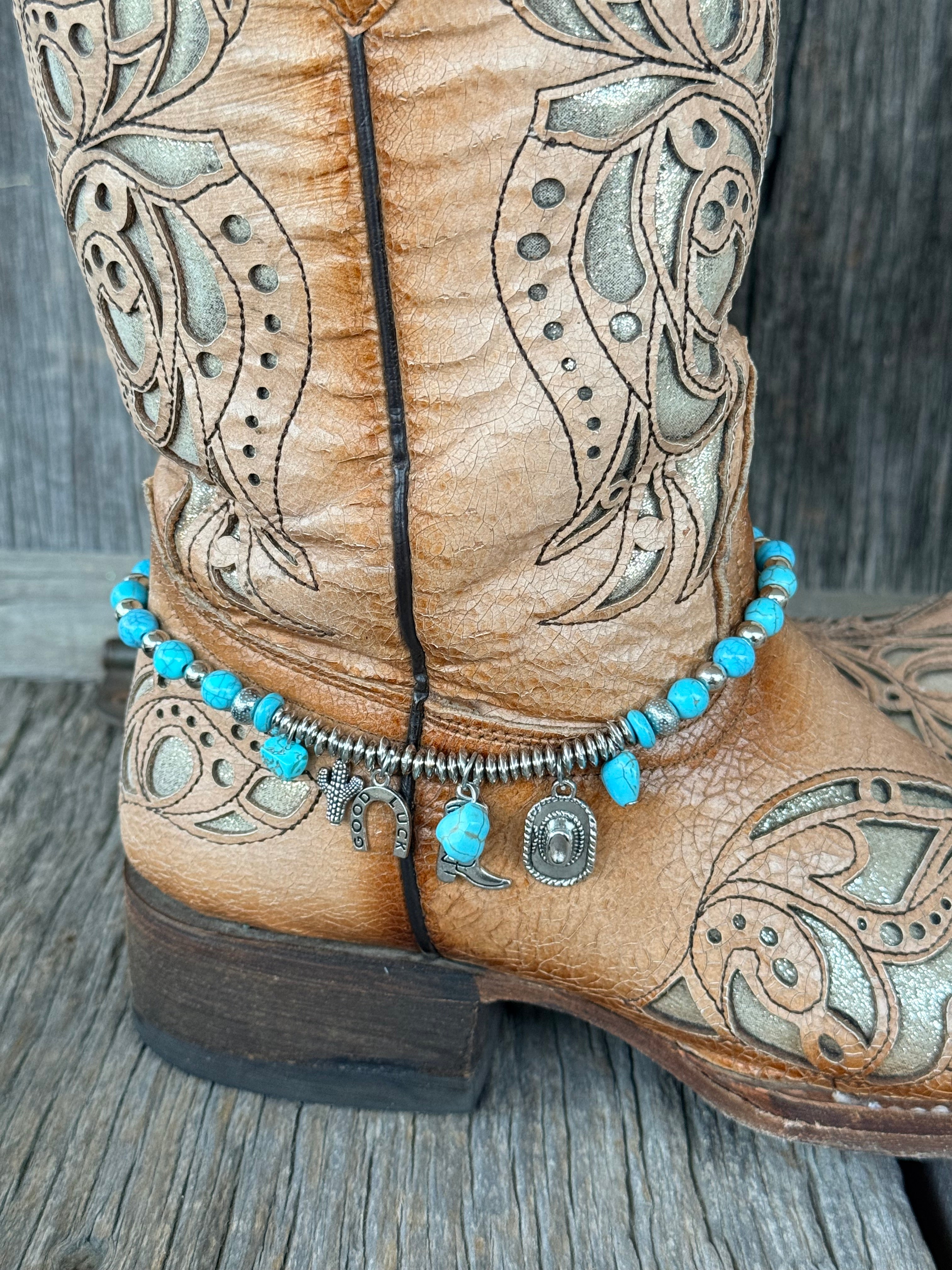 Close-up of turquoise round bead and silver rondelle spacer boot bracelet with six-charm cluster including cactus, Good Luck horseshoe, cowboy boot, turquoise stone chip, turquoise bead and cowboy hat charms at heel of tan tooled cowboy boot
