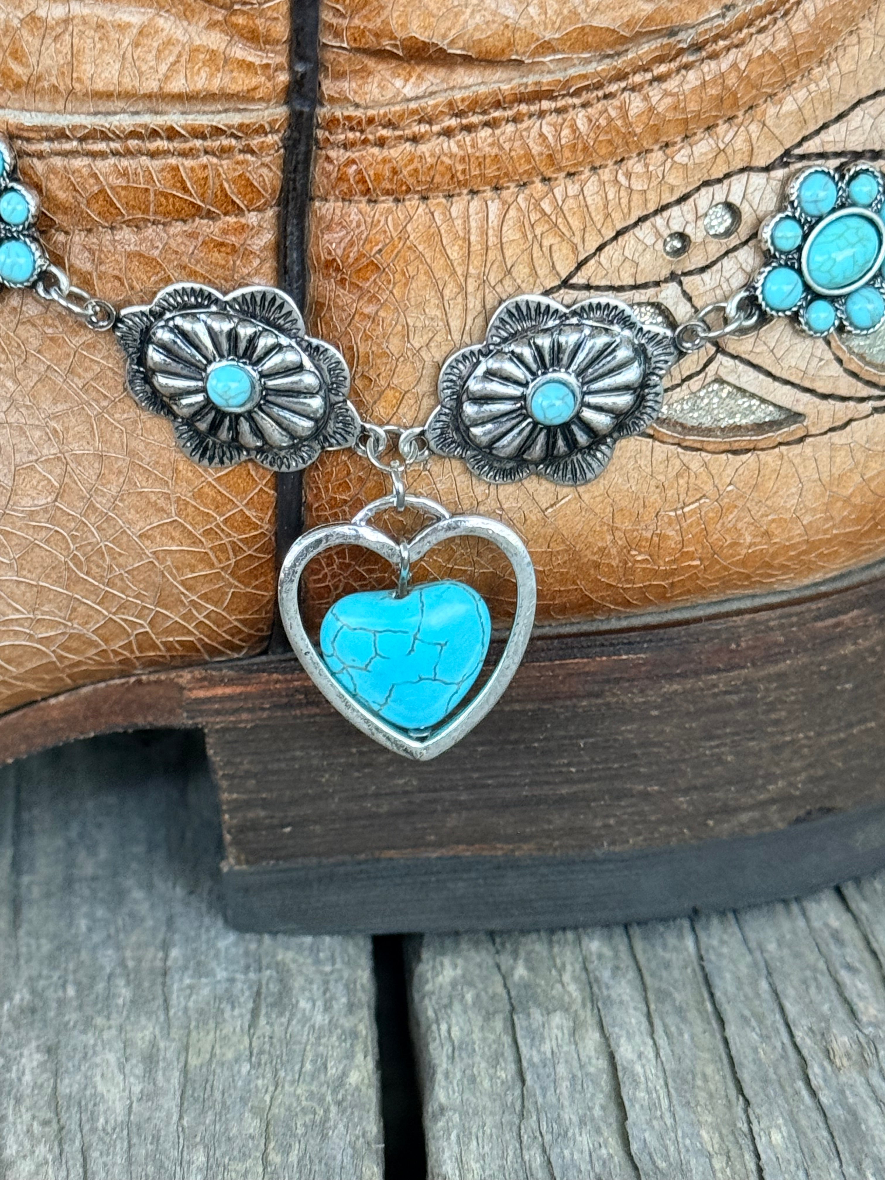Detail view of large open silver heart frame pendant with full turquoise stone heart drop and silver scalloped flower conchos with turquoise cabochon centers on boot bracelet chain
