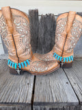 Turquoise coyote tooth and bull skull boot bracelet worn on tan tooled leather cowboy boots, full pair view
