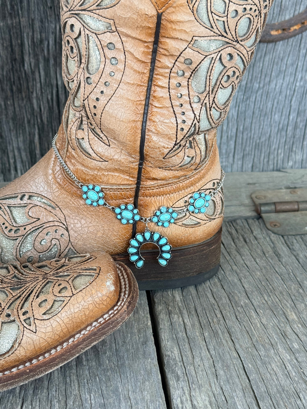 Side view of turquoise cluster rosette boot bracelet chain draped along tan cowboy boot shaft
