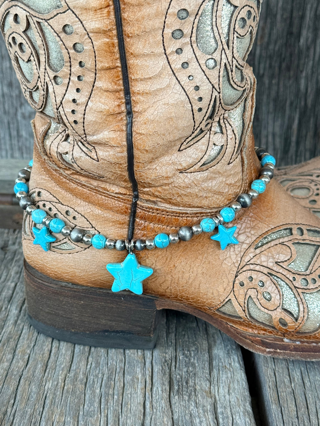 Close-up of Navajo pearl silver round bead and turquoise bead boot bracelet with large center turquoise star stone pendant and two smaller flanking turquoise stars at heel of tan tooled cowboy boot
