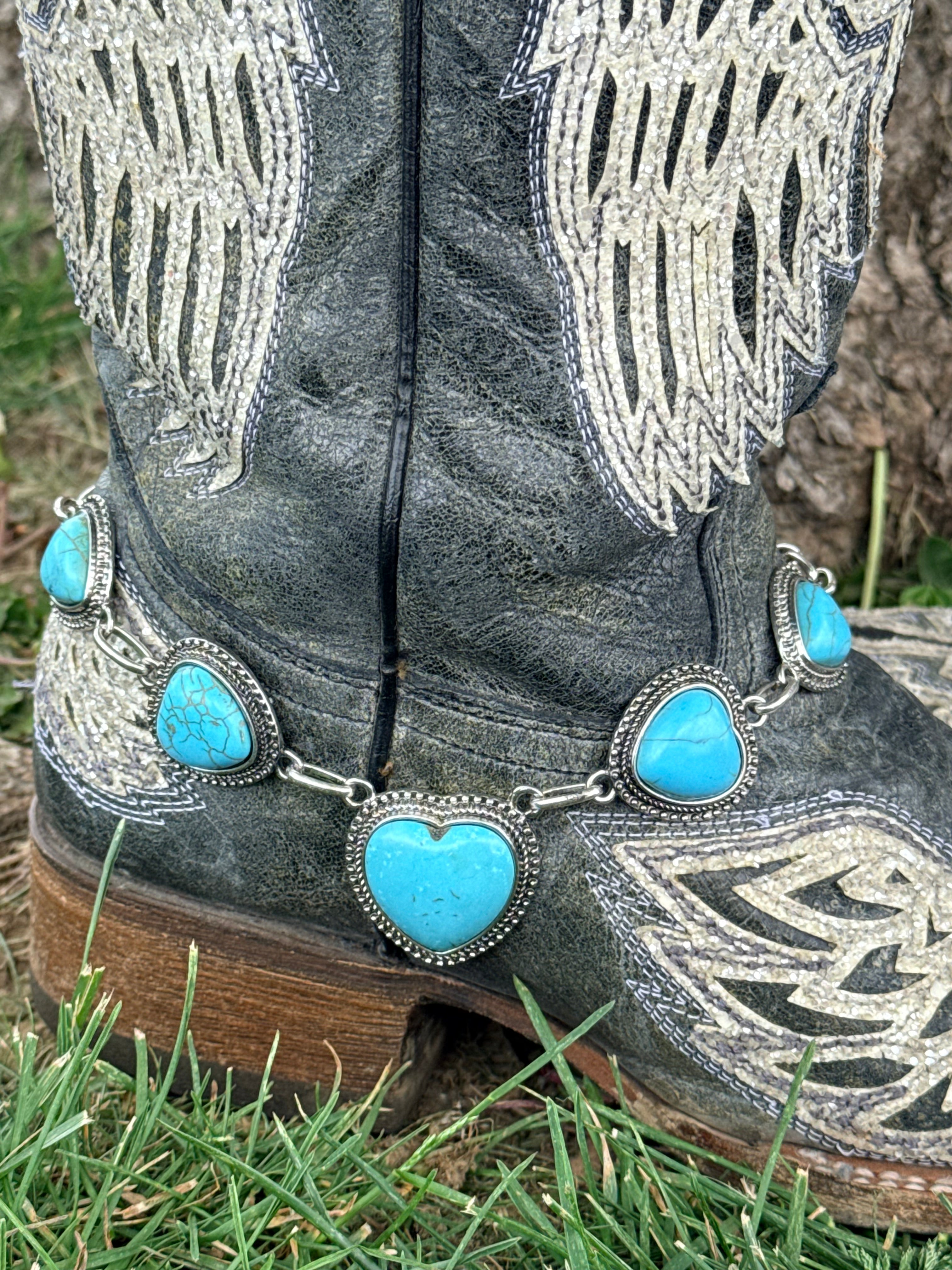Close-up of turquoise howlite heart boot bracelet with large center heart stone, medium heart side stones, and smaller accent heart stones in silver beaded bezels linked by a silver chain on black angel wing cowboy boots
