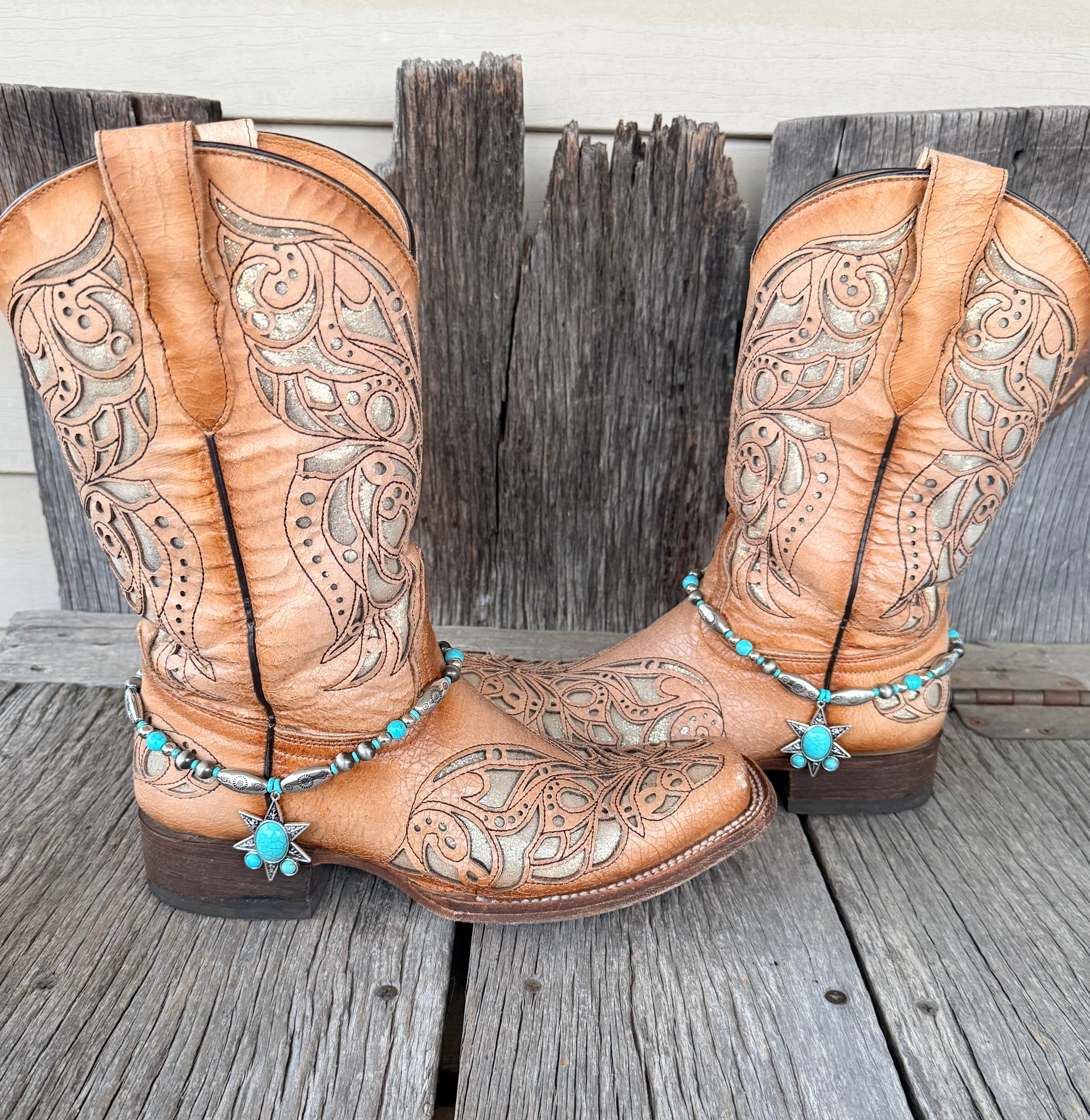 Turquoise and silver 8-point star boot bracelet with engraved silver barrel beads and large star pendant worn on tan tooled laser-cut cowboy boots, full pair front view on wood surface
