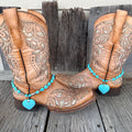 Turquoise heart bead boot bracelet with large crackle turquoise heart stone pendant worn on tan tooled laser-cut cowboy boots, full pair front view against weathered wood
