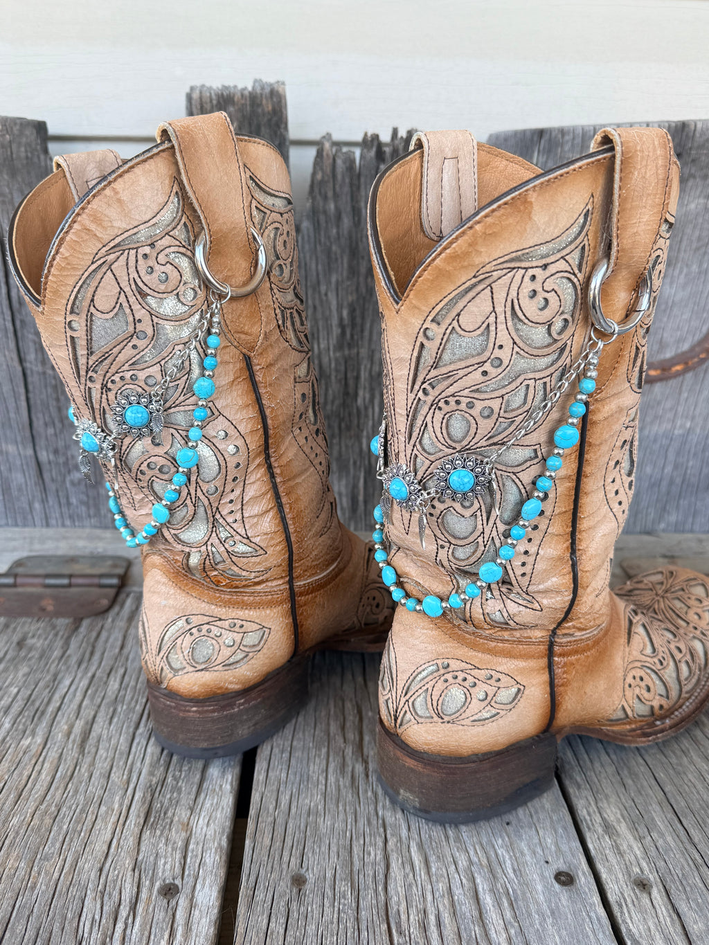 Back view of silver flower concho and turquoise beaded boot bracelet chain clipped through pull loop ring on tan tooled laser-cut cowboy boots
