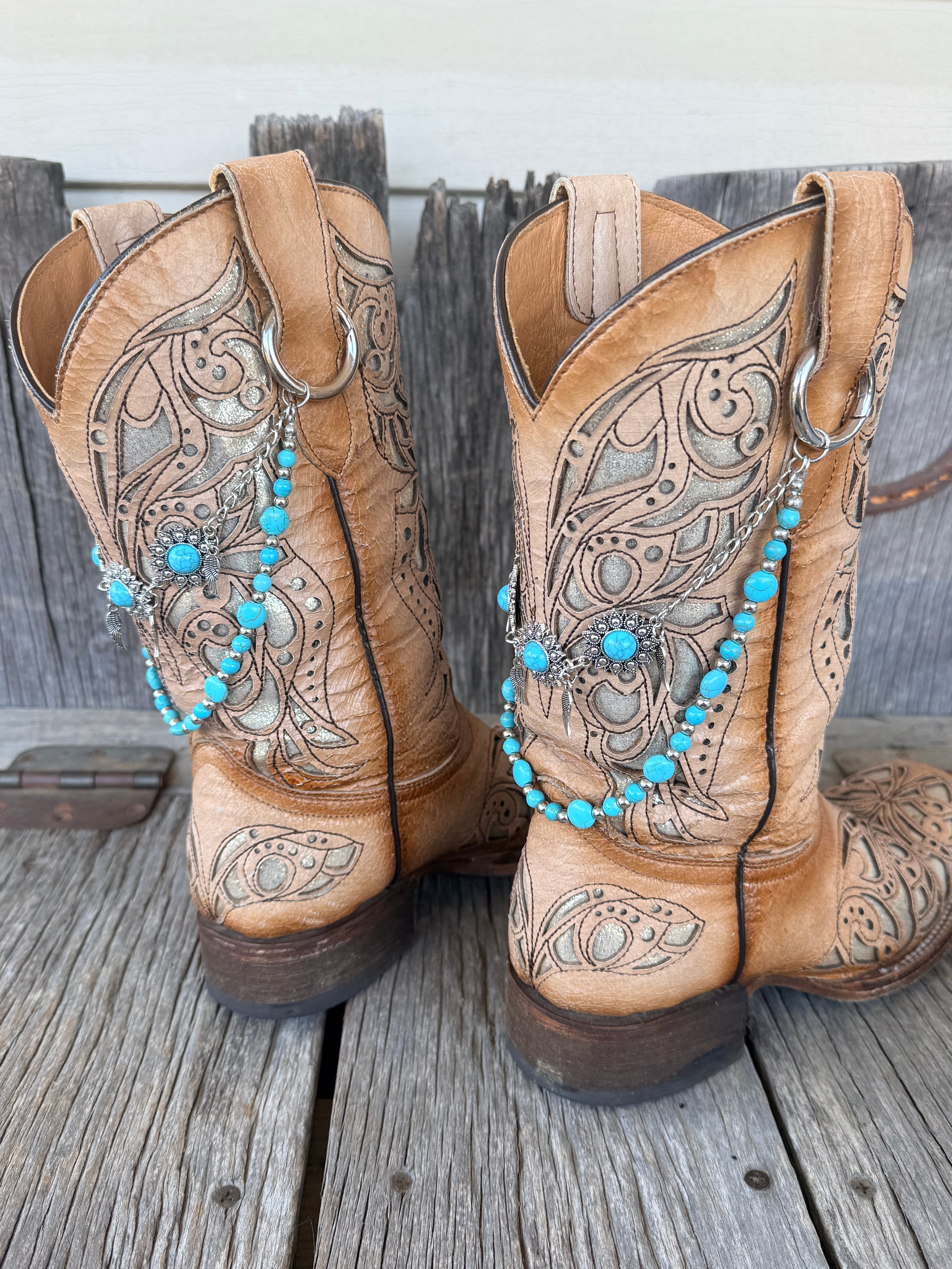 Back view of silver flower concho and turquoise beaded boot bracelet chain clipped through pull loop ring on tan tooled laser-cut cowboy boots
