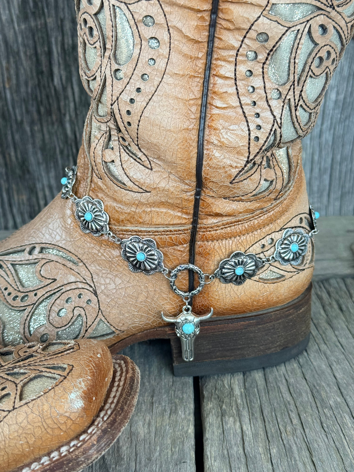 Side angle of turquoise concho boot bracelet chain with bull skull drop pendant draped along tan tooled leather cowboy boot shaft

