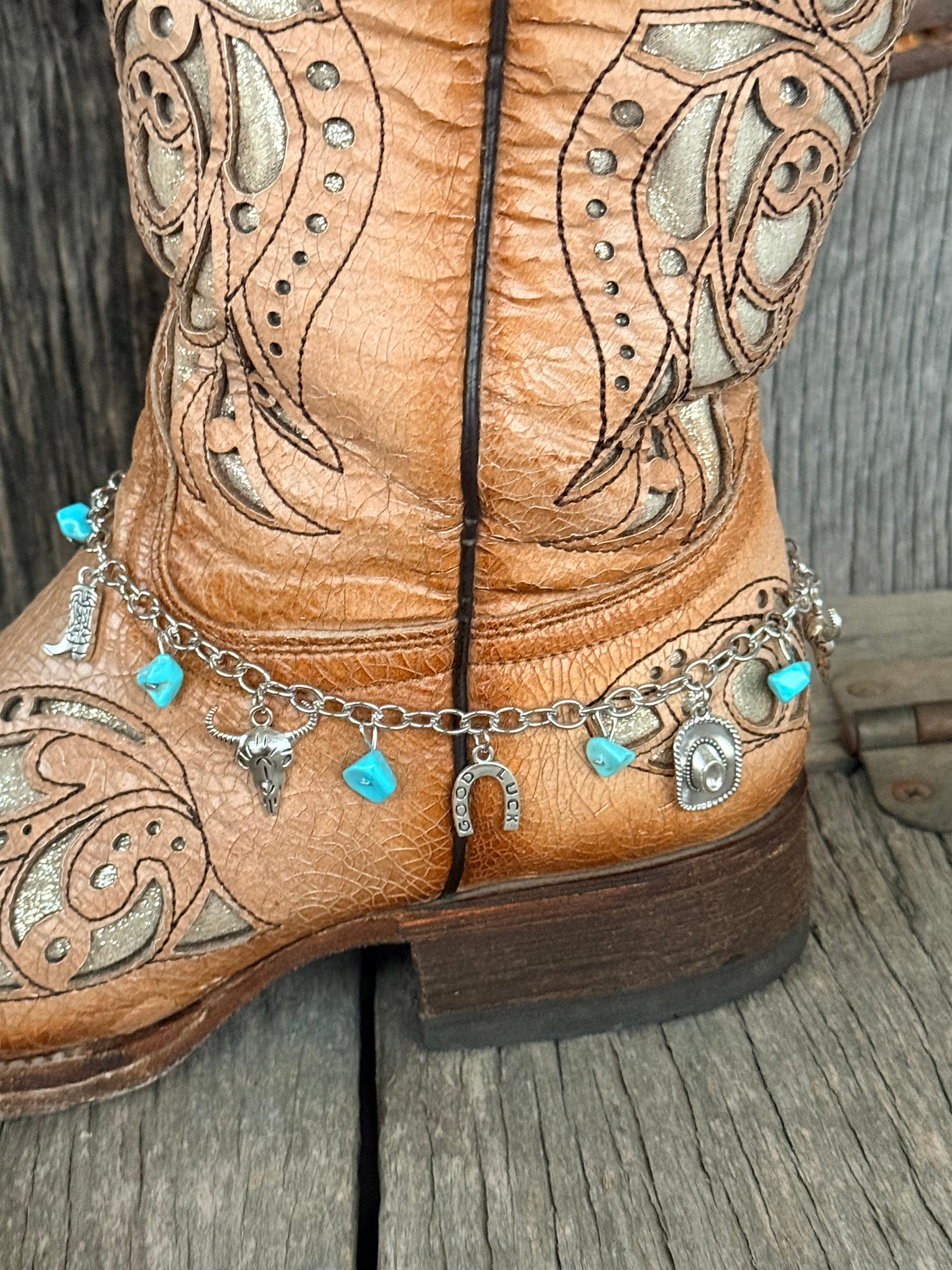Side view of silver curb chain Western charm boot bracelet with turquoise stone chips and silver cowboy boot, steer head, Good Luck horseshoe, and cowboy hat charms draping at ankle of tan tooled cowboy boot
