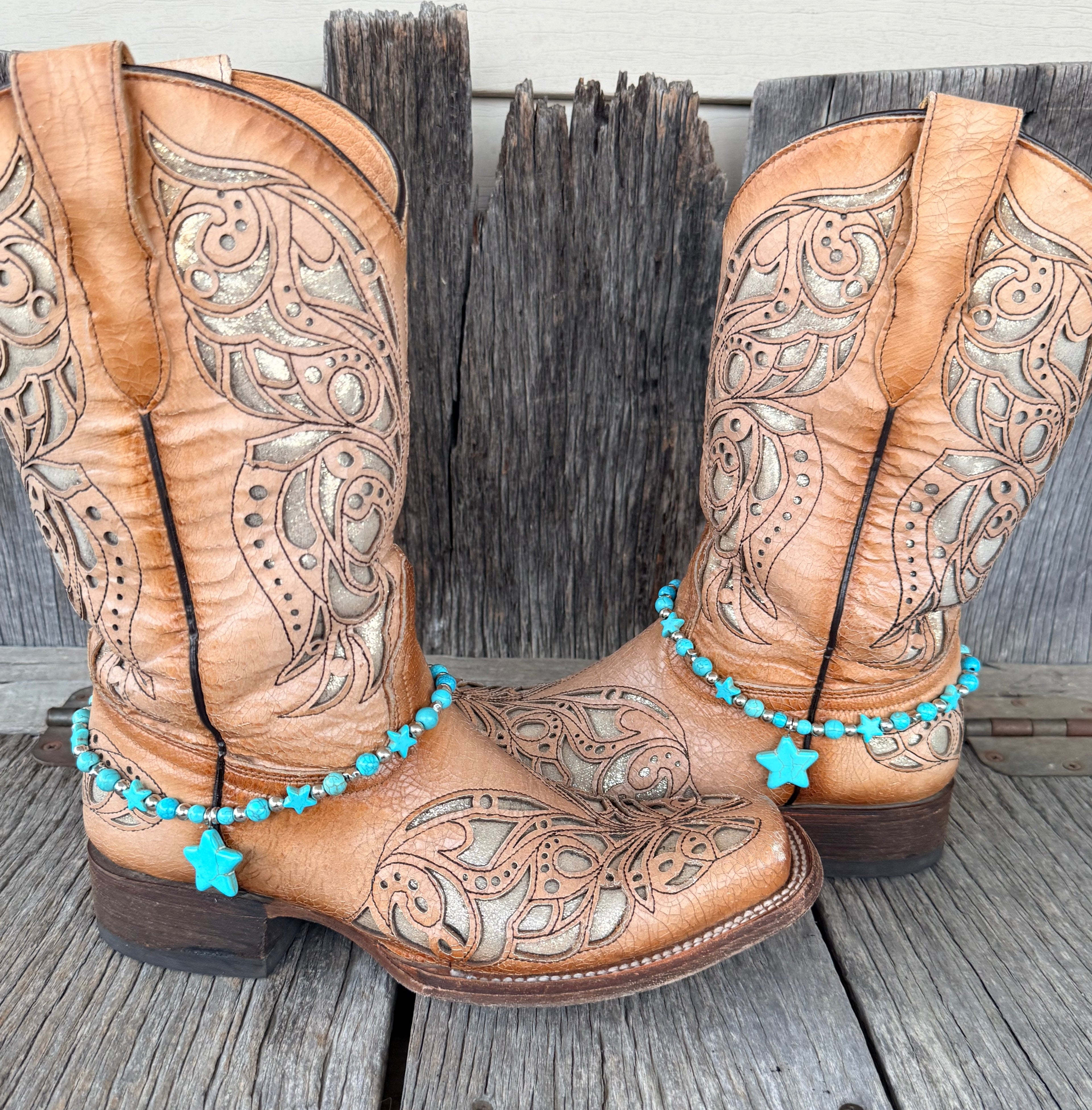 Turquoise star beaded boot bracelet with multiple turquoise star beads and large center star pendant worn on tan tooled laser-cut cowboy boots, full pair front view on wood surface
