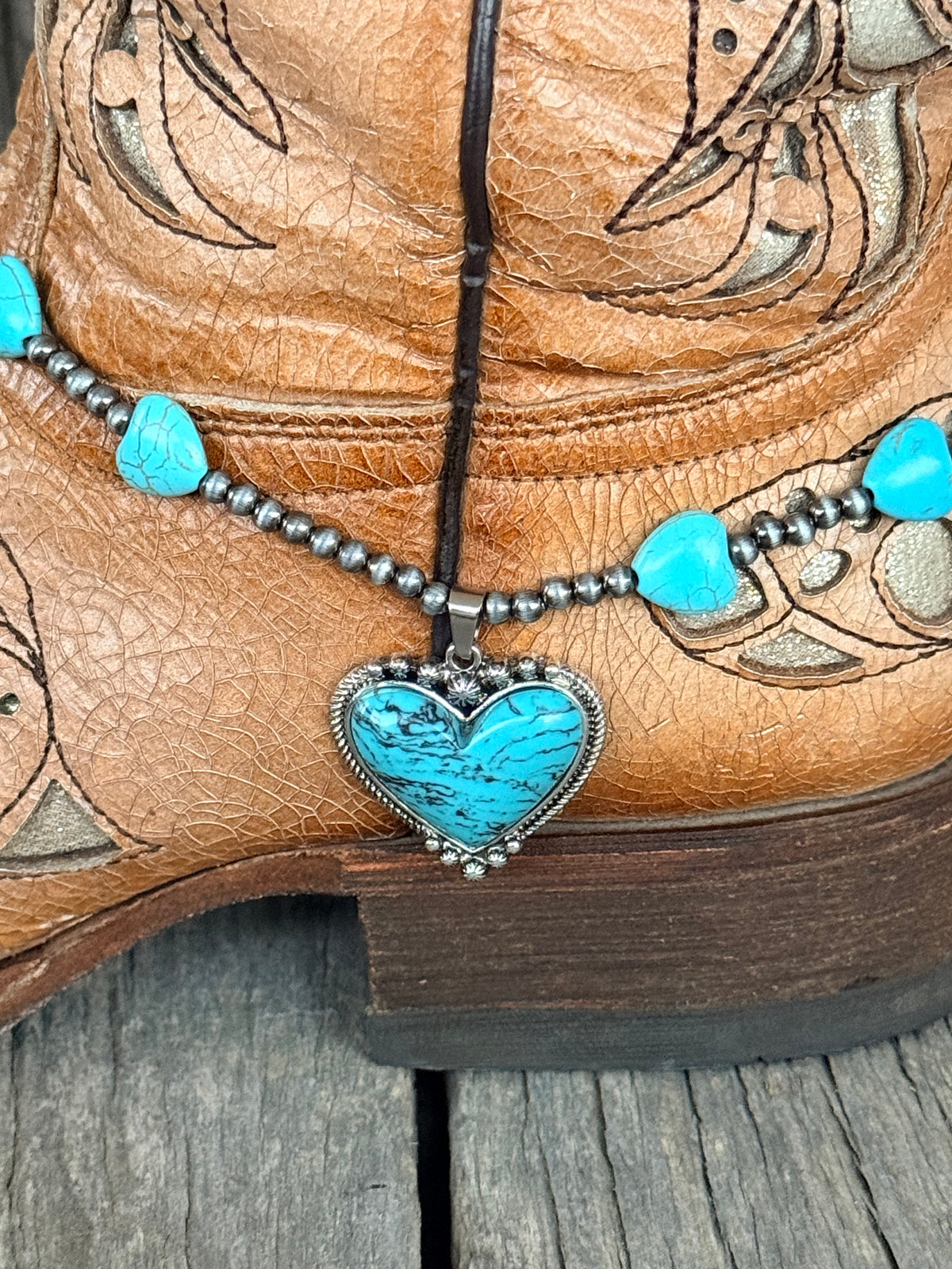 Detail close-up of large turquoise heart stone pendant with rope-twist silver border, silver star accent at top, and silver dot edge detail on turquoise heart bead and Navajo pearl gunmetal bead boot bracelet
