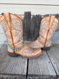 Turquoise bead and silver charm boot bracelet with Good Luck horseshoe and Western charm cluster worn on tan tooled laser-cut cowboy boots, full pair front view on wood surface
