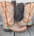 Turquoise star and Navajo pearl silver bead boot bracelet with three turquoise star stone pendants worn on tan tooled laser-cut cowboy boots, full pair front view on wood surface
