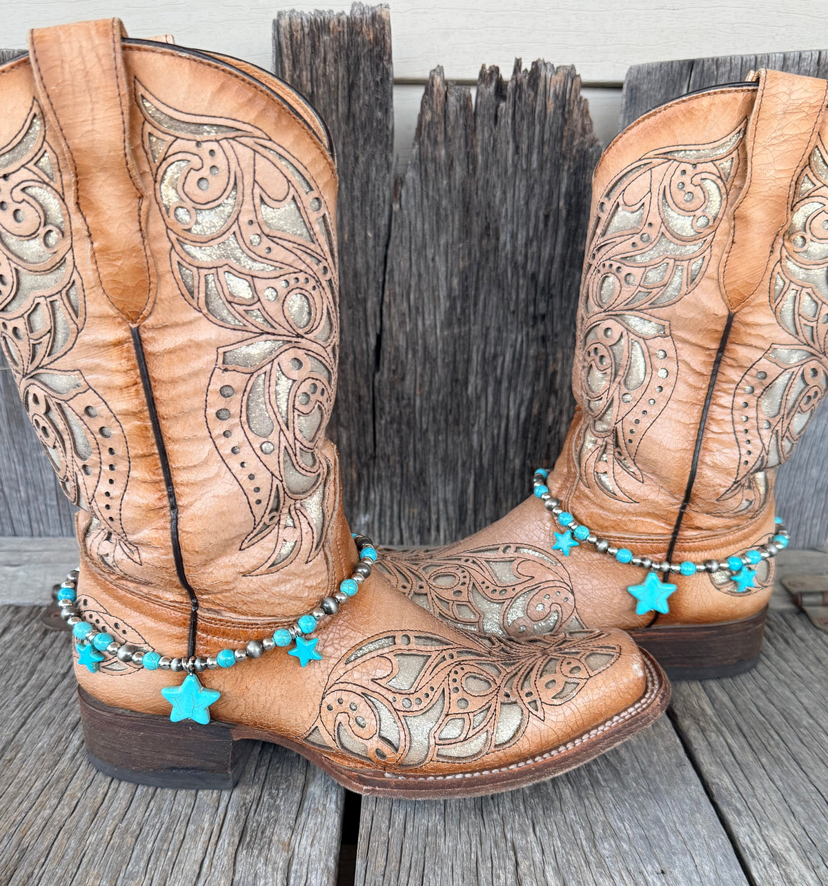 Turquoise star and Navajo pearl silver bead boot bracelet with three turquoise star stone pendants worn on tan tooled laser-cut cowboy boots, full pair front view on wood surface
