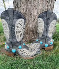 Turquoise heart boot bracelet with silver beaded bezel chain draped across the toe of black angel wing embroidered cowboy boots resting against a tree outdoors
