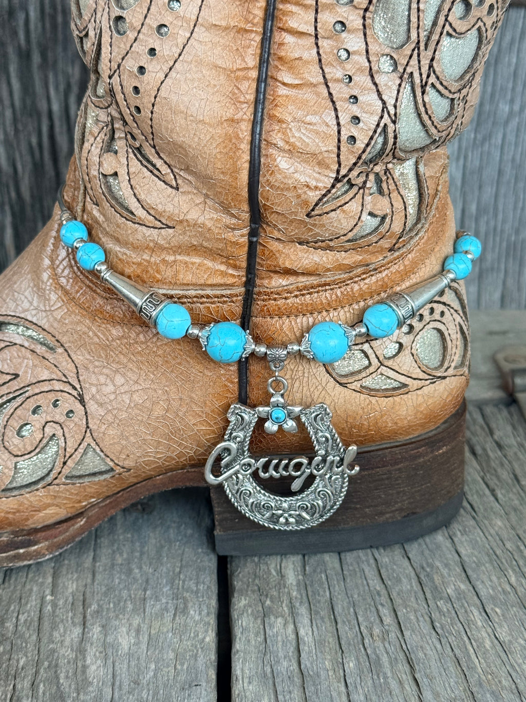 Side view of turquoise bead and silver butterfly spacer boot bracelet with ornate Cowgirl horseshoe pendant draping at ankle of tan laser-cut tooled cowboy boot

