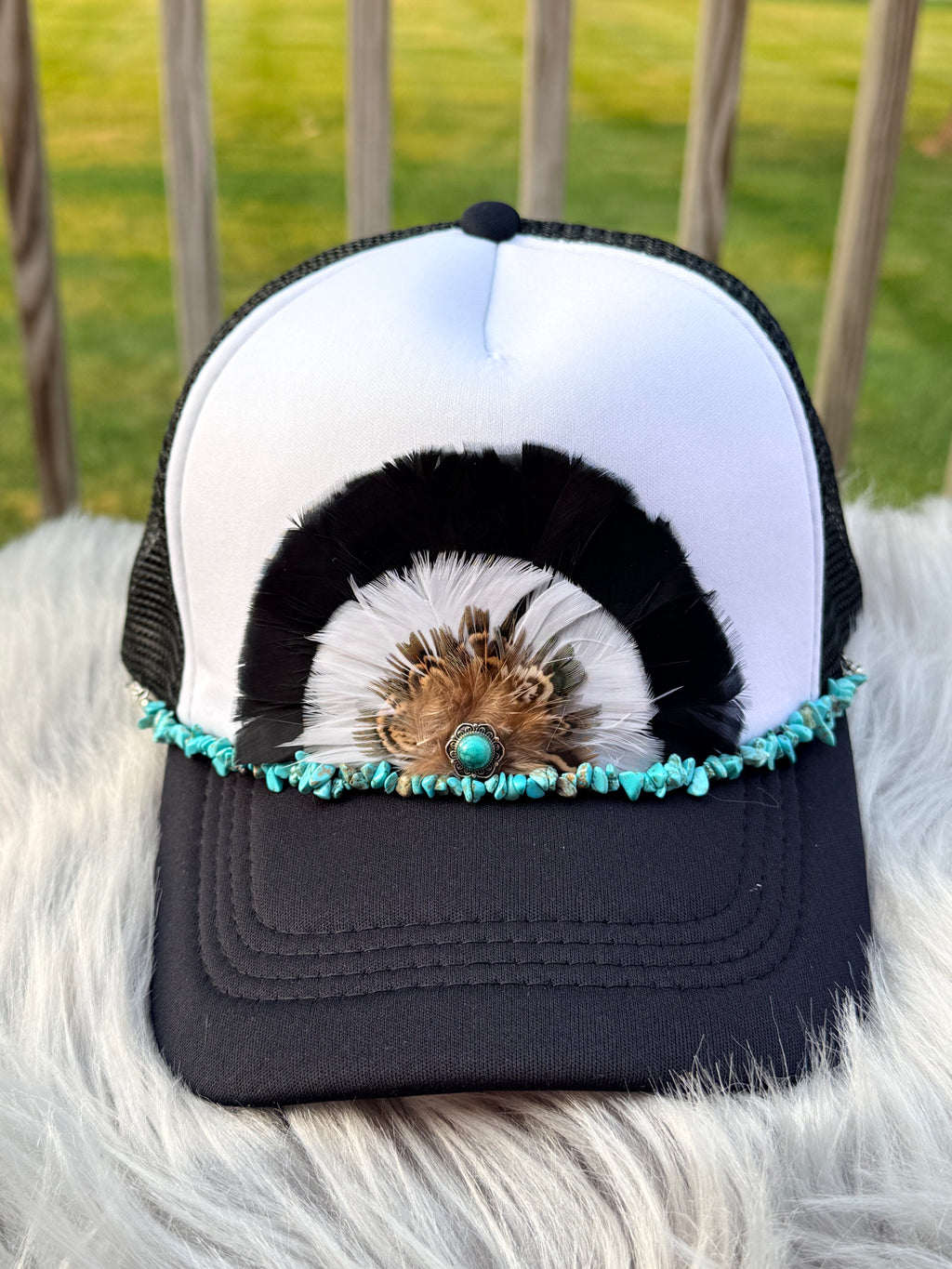 A black and white trucker hat with a decorative feather and turquoise bead embellishment on the brim,
