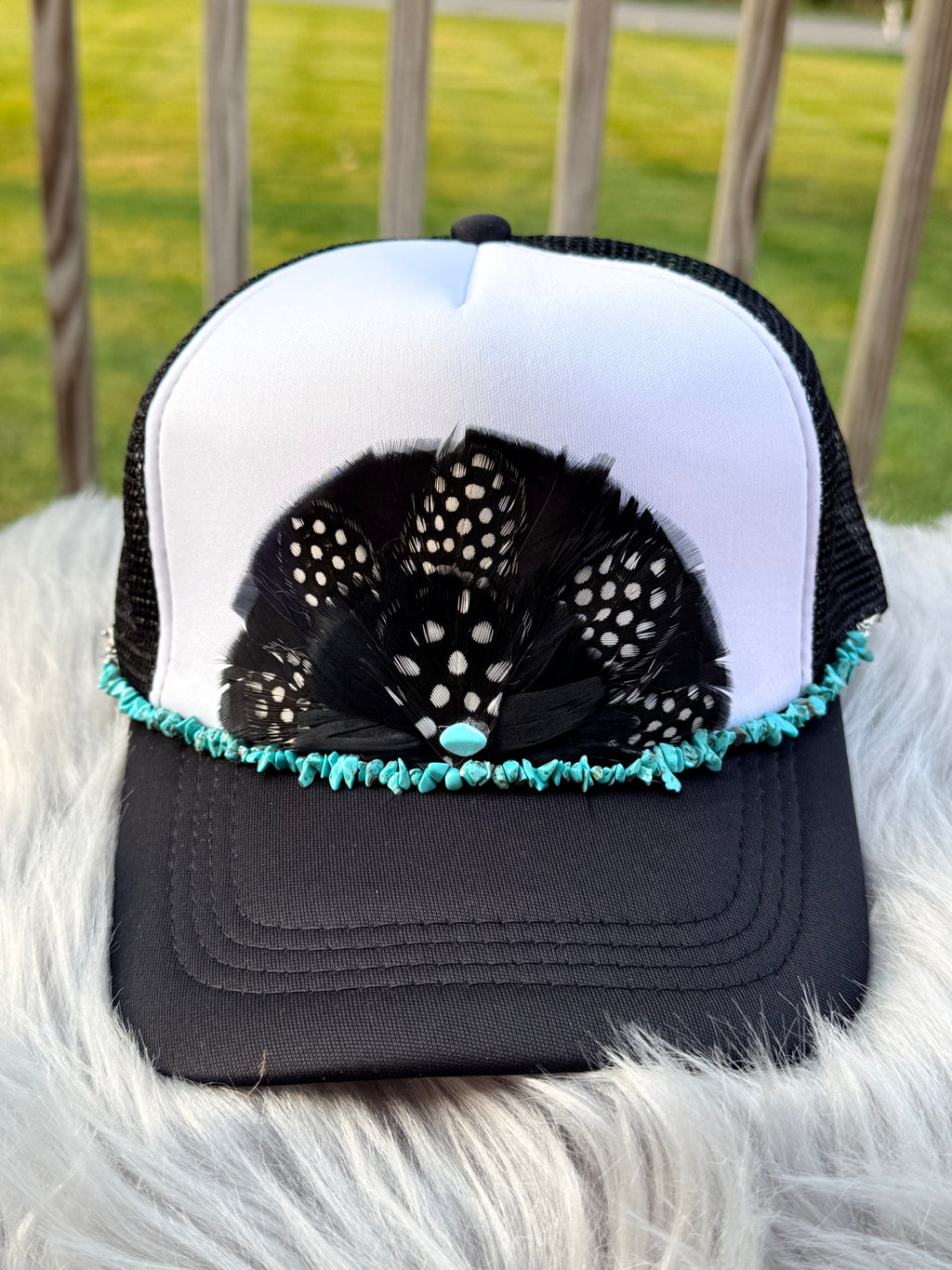 A black and white trucker hat with a decorative black feather fan, turquoise beaded trim, and a turquoise center bead,