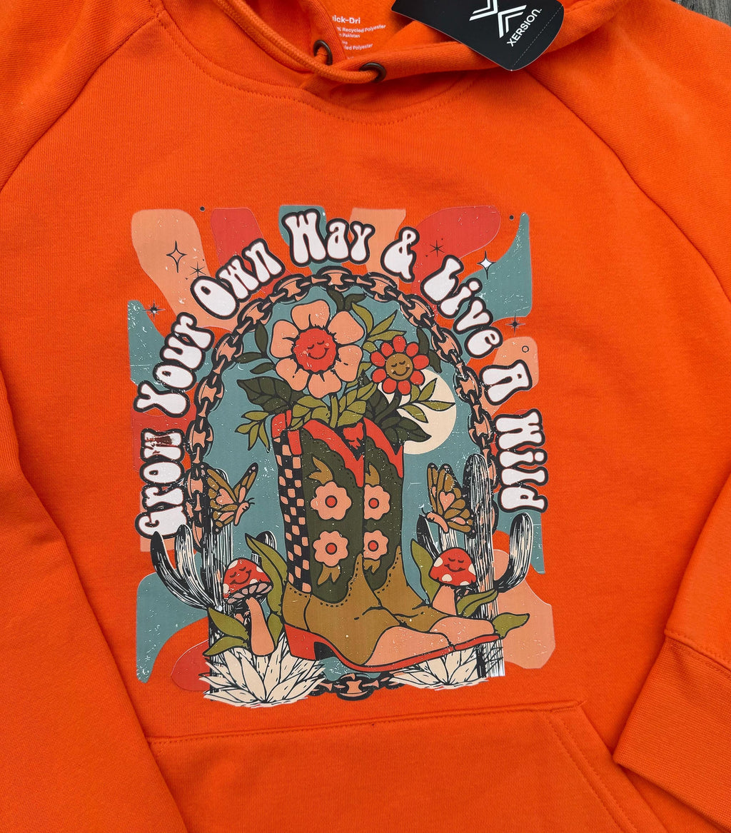 Close-up of an orange hoodie featuring a colorful retro-style graphic print on the chest with flowers, mushrooms, butterflies.