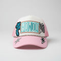 A pink and white trucker hat with 'HOWDY' embroidered in teal on the front, decorated with patches, a silver chain across the brim, and a rhinestone star on the pink brim.