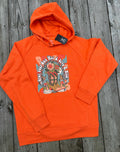 Bright orange pullover hoodie laid flat on a weathered gray wooden plank surface, featuring a large colorful front graphic with floral artwork and stylized text.