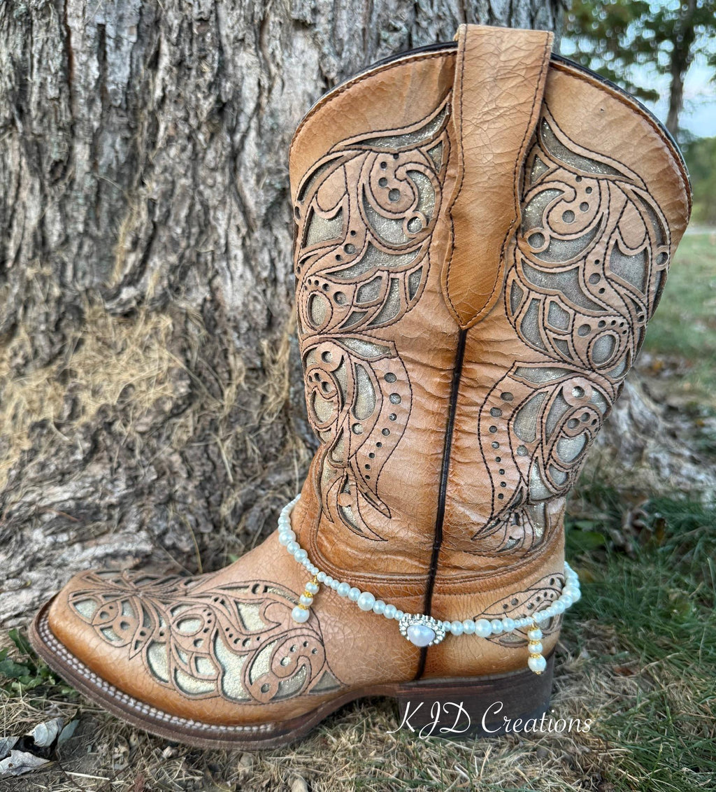 Side view of tan tooled leather cowboy boot against tree trunk wearing pearl and crystal beaded boot bracelet with rhinestone concho charm, bridal Western style