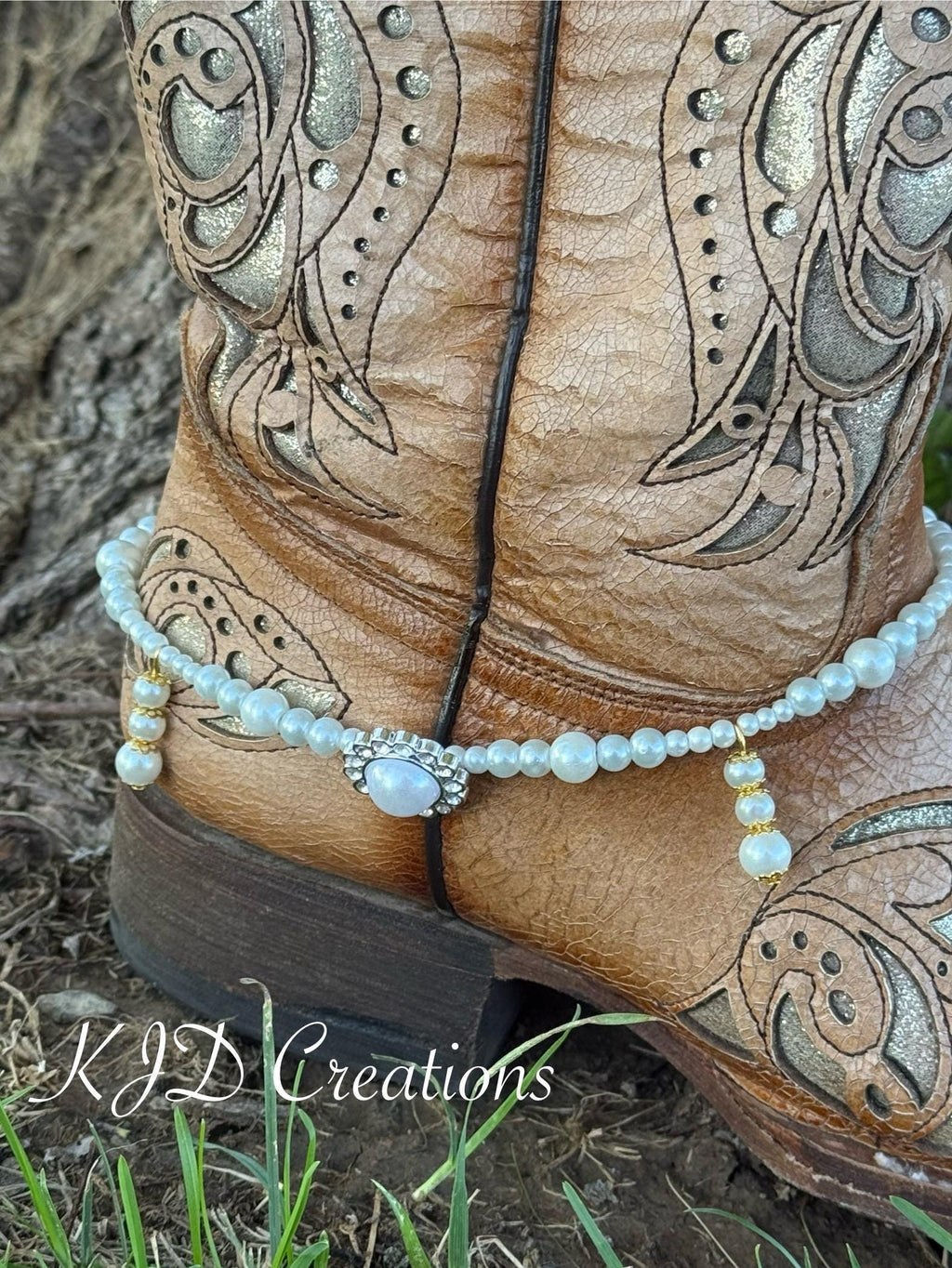 Back heel close-up of pair of tan tooled leather cowboy boots wearing pearl beaded boot bracelets with rhinestone and pearl oval concho charm, Western bridal boot jewelry