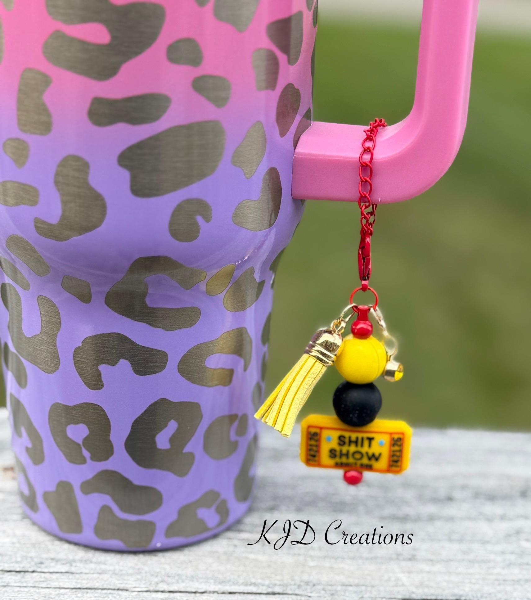 Admit One country music tumbler cup handle charm clipped to a pink and purple leopard print insulated tumbler — yellow and black beads with yellow tassel on red chain