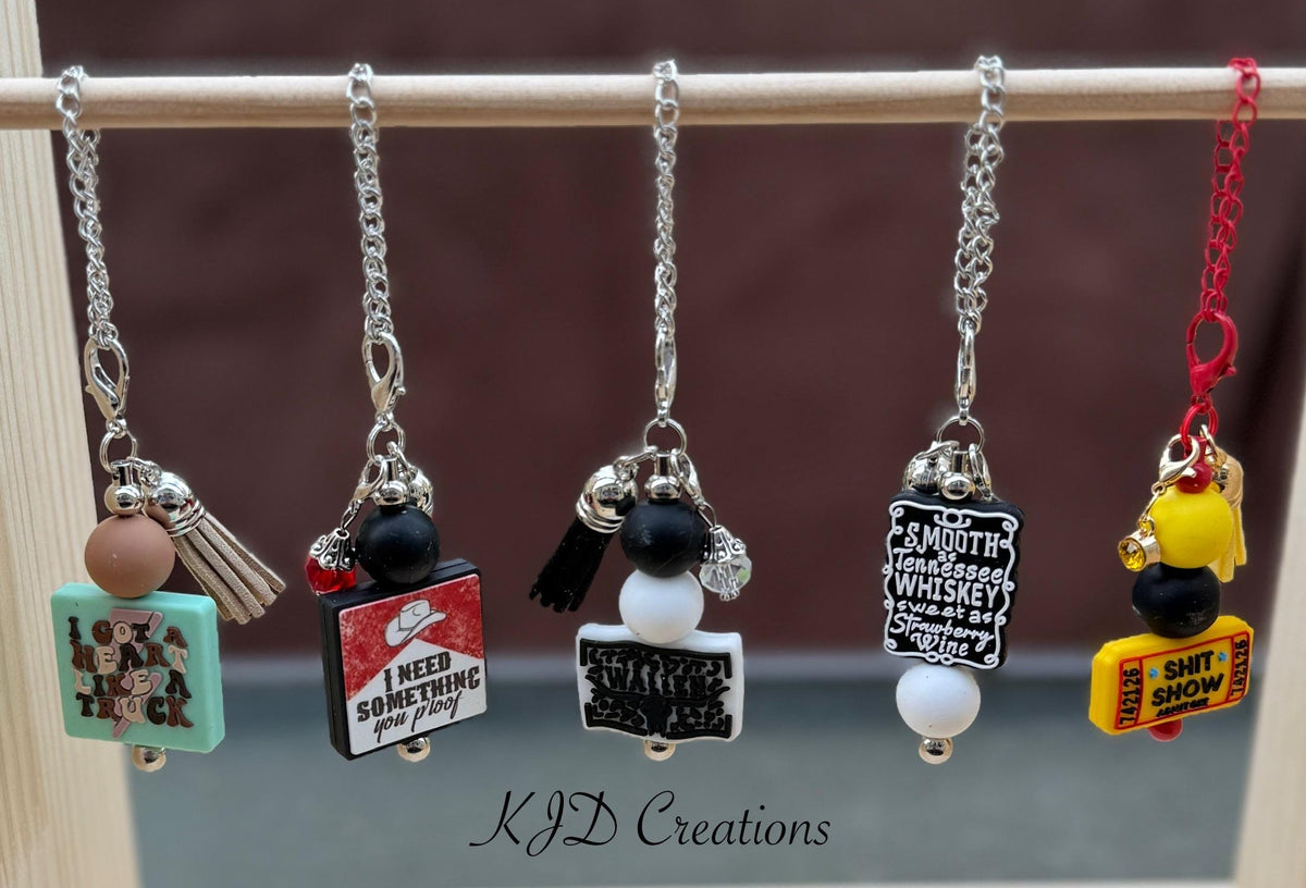 Five country music tumbler cup handle charms clipped to a pink and purple leopard print insulated tumbler — You Proof, Whiskey, Admit One, Country Singer, and Truck 