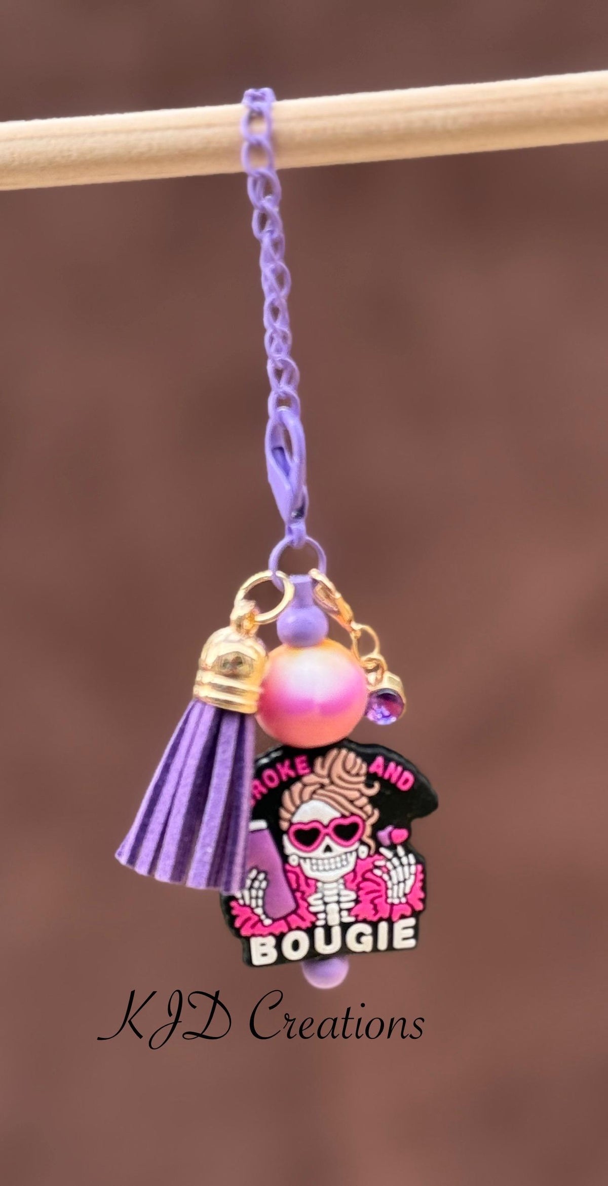 Bougie and Broke purple silicone beaded tumbler charm with sassy skull pendant and purple leather tassel on purple chain, hanging from a pink and purple leopard print tumbler handle
