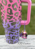 Bougie and Broke purple silicone beaded tumbler charm with sassy skull pendant and purple leather tassel on purple chain, hanging from a pink and purple leopard print tumbler handle