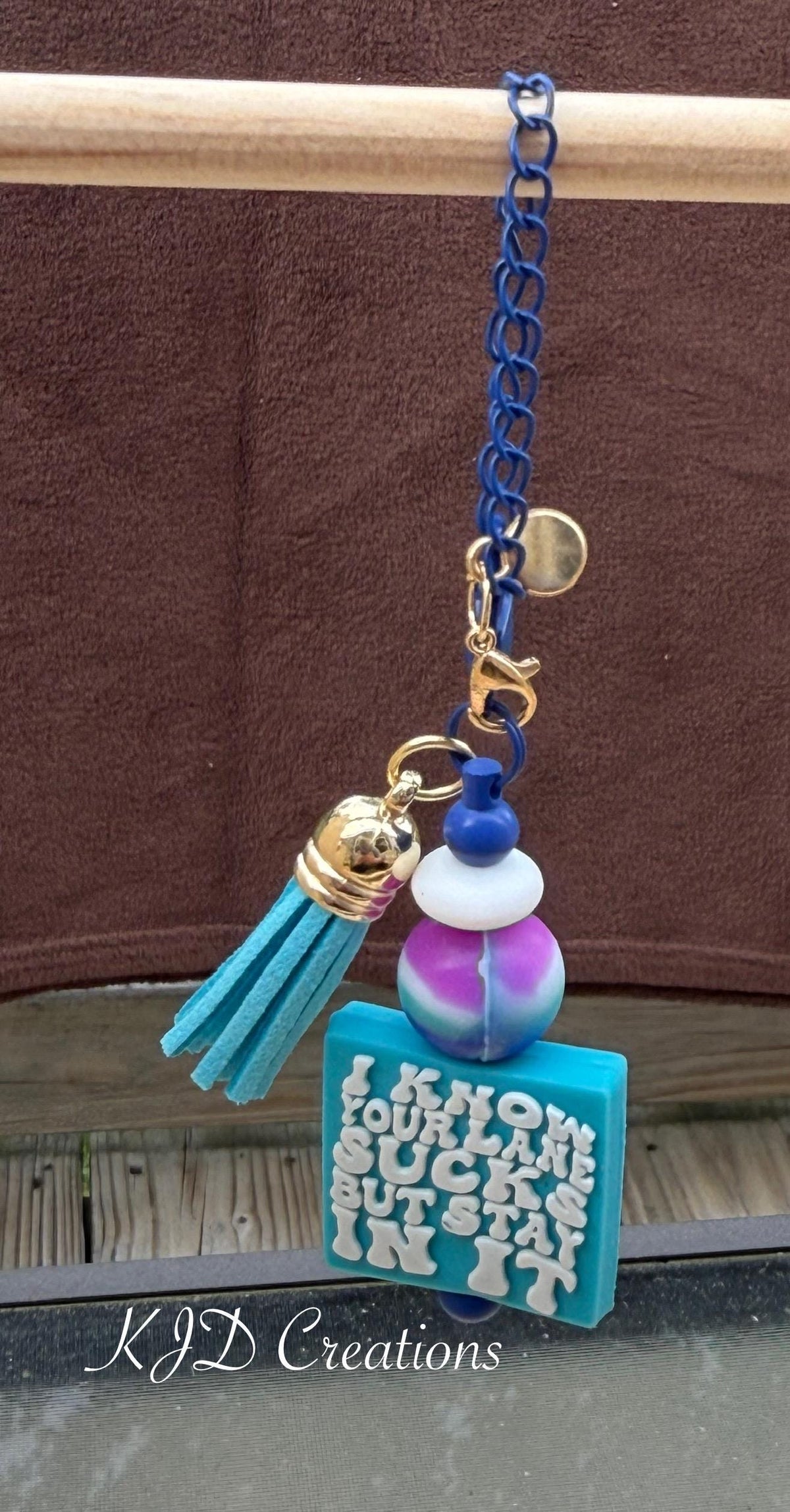Stay In Your Lane tumbler charm close-up on display rack — navy blue chain with teal leather tassel, tie-dye silicone bead, and teal square charm reading "I Know Your Lane Sucks But Stay In It" by KJD Creations