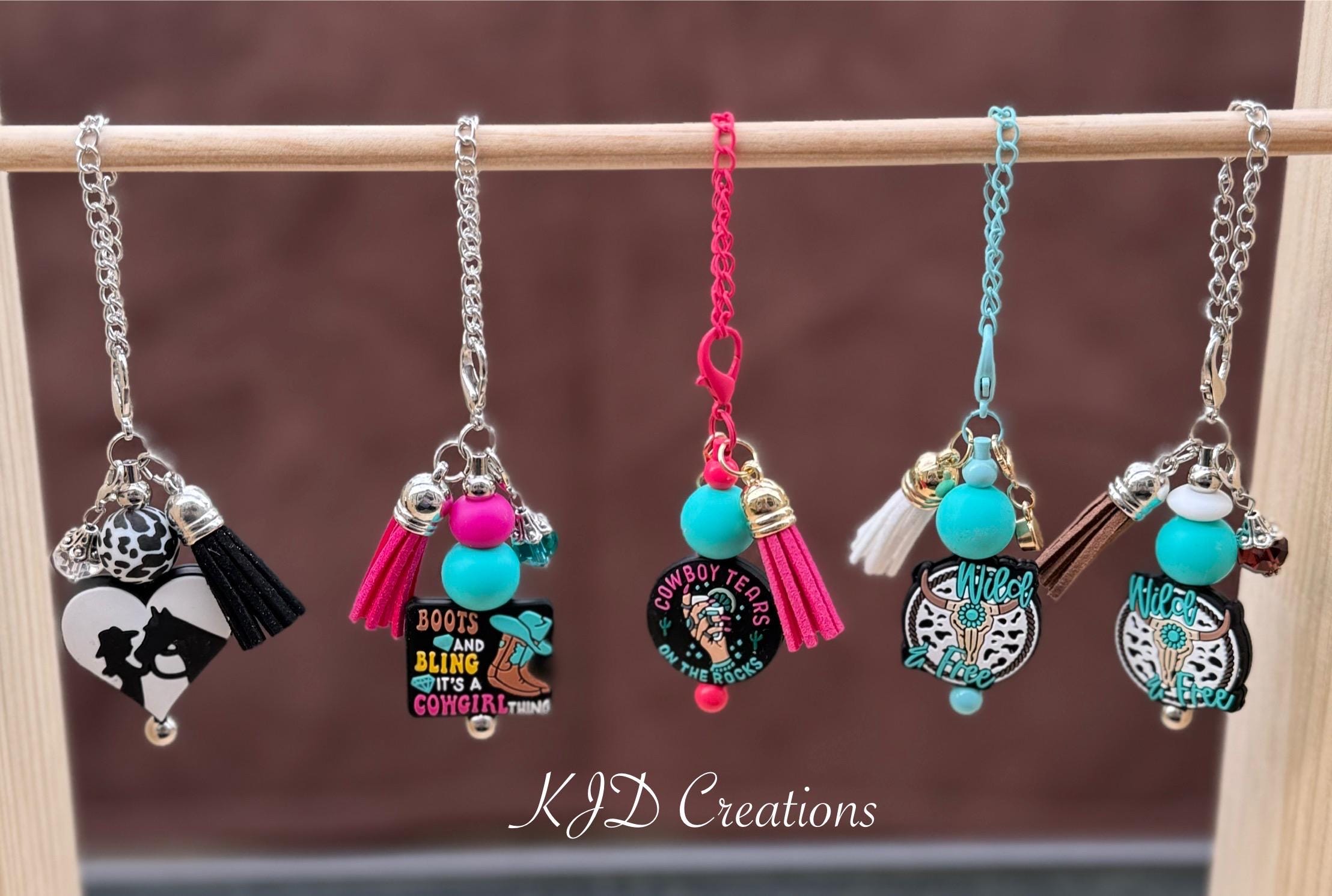Five Western silicone beaded tumbler dangle charms on a display rack — Cowgirl Horse, Boots Bling, Cowboy Tears, and two Wild & Free longhorn designs by KJD Creations