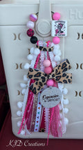 Expensive Difficult & Talks Back silicone beaded bag tassel with leopard print bow, glitter Expensive & Difficult charm disc, white pom-pom trim, and layered hot pink ribbon tassel clipped onto a white Hurley tote bag
