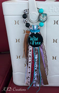 Western cowgirl bag tassel with Wild & Free charm disc, mixed ribbon fringe, leather tassel, and silicone beads clipped to a white Bogg-style bag