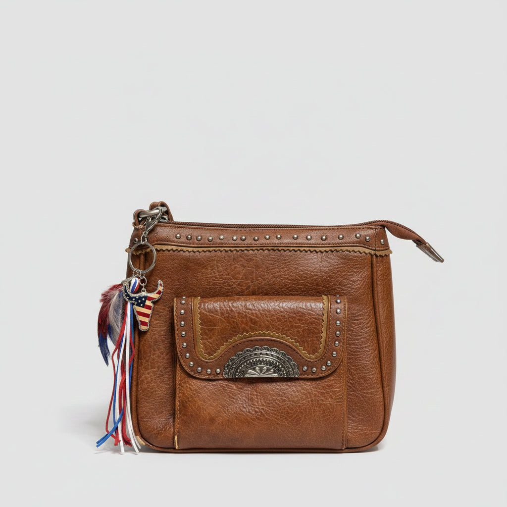 Stars & Stripes Western boho purse charm clipped to brown studded Western crossbody bag zipper featuring rhinestone-bordered American flag longhorn steer charm, red white and blue marabou and guinea fowl feather bundle, and red white and blue suede leather fringe tassel strands on silver key ring